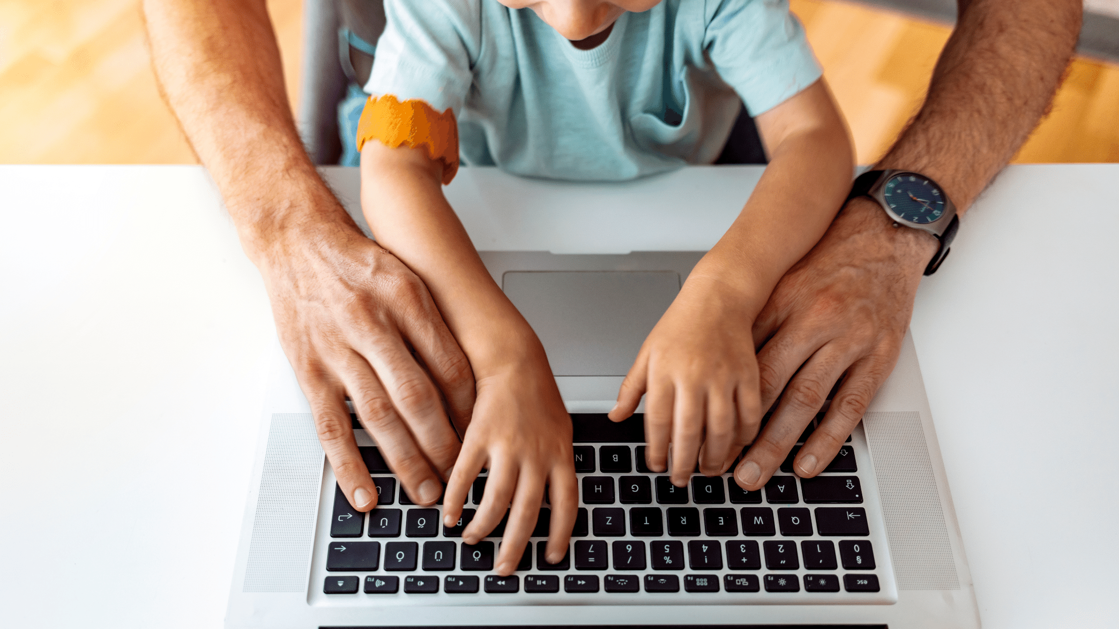 A man and a child engaged in backup child care, typing on a laptop.