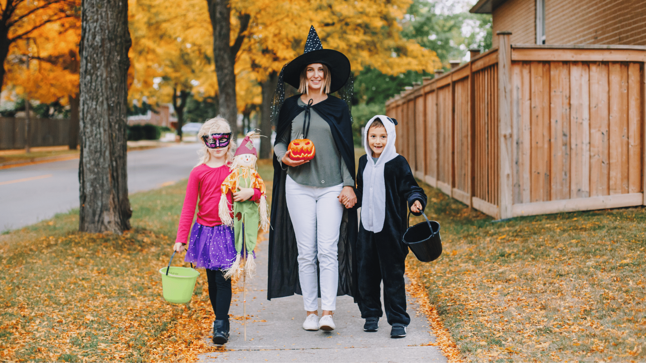 A woman dressed as a witch and her children walking down a sidewalk, ensuring safety.