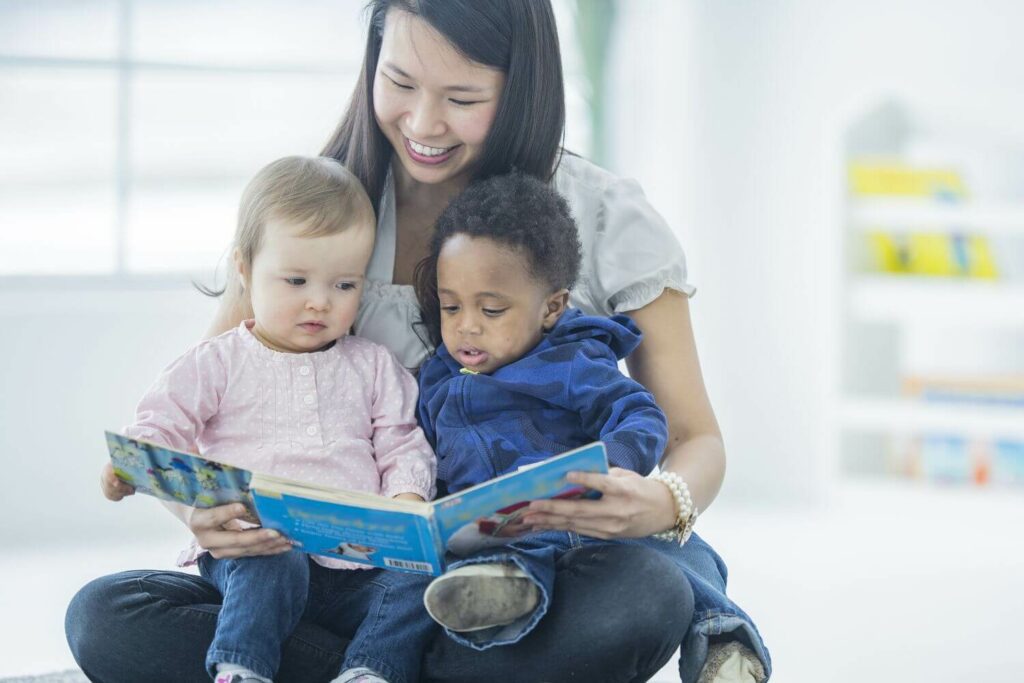 A woman is reading a book to two infants.