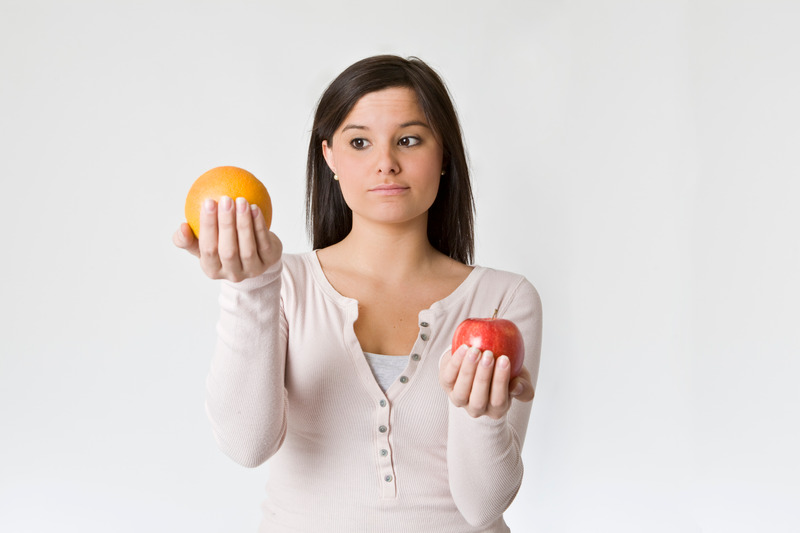 A woman holding an orange and an apple trying to decide between two different child care options