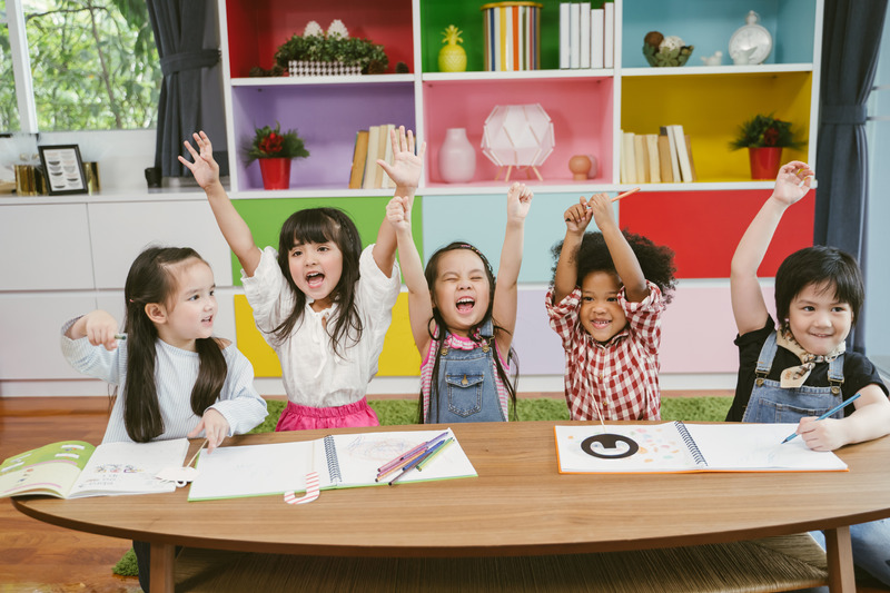 A group of children are sitting at a table, engaging in a stimulating activity and eagerly raising their hands.