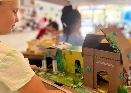 A young child observes cardboard house models at a school project exhibition.
